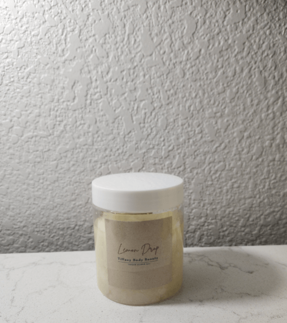 Lemon Drop Body Buffer scrub jar on a marble surface with a textured background.